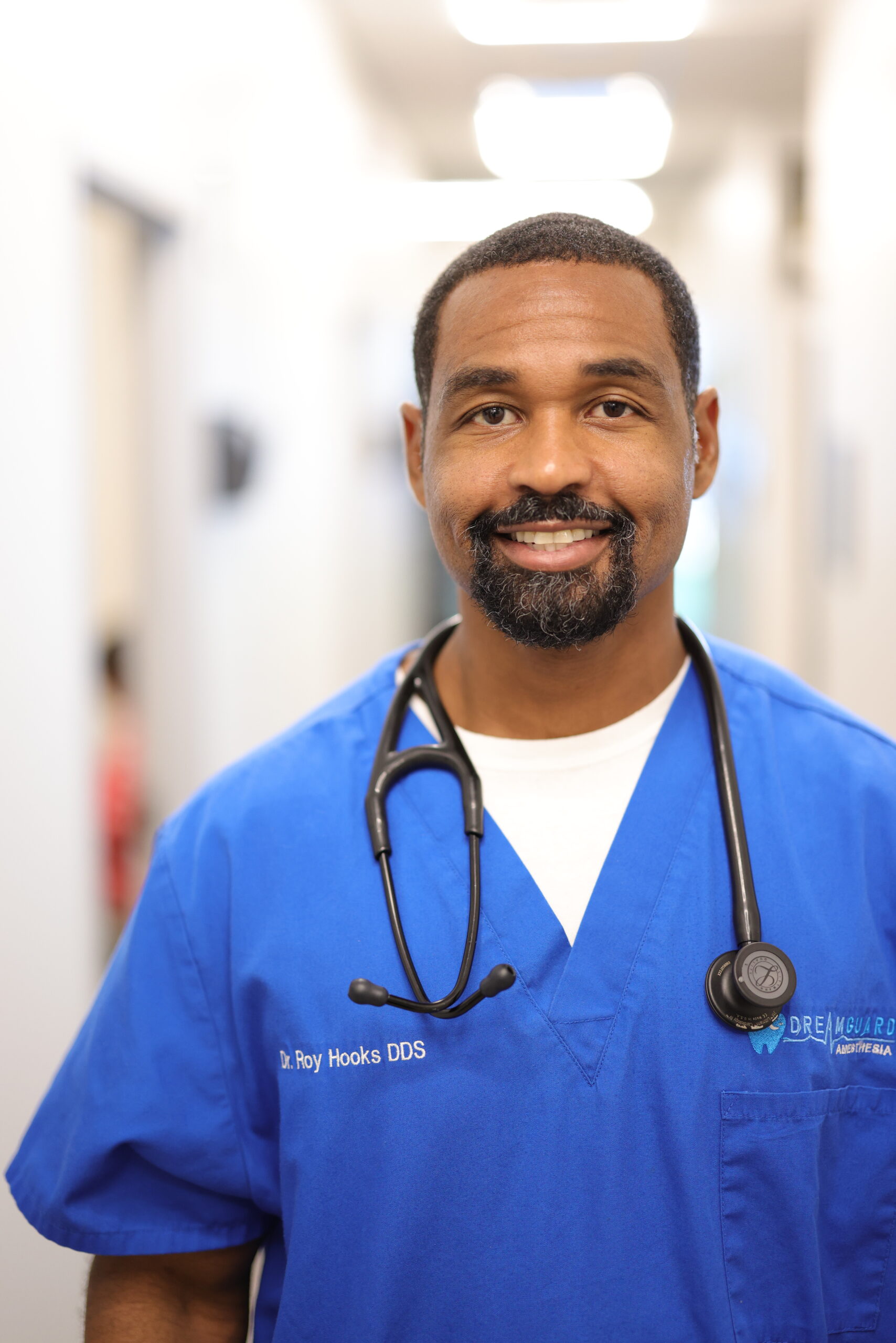 Smiling male doctor wearing blue scrubs and stethoscope.